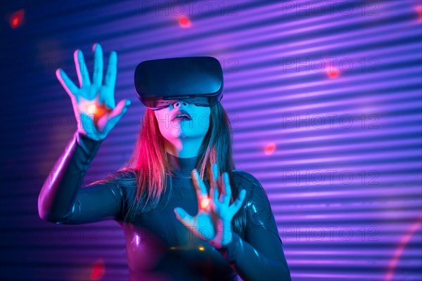 Woman during an interactive game with VR goggles in an urban night space with neon lights