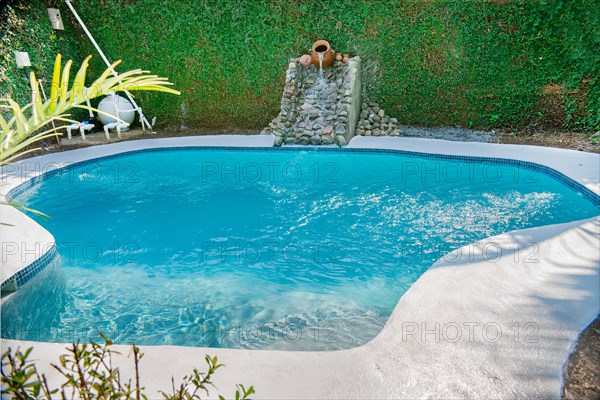 Swimming pool designs for the home. Crystal water home pool surrounded by a garden. Home swimming pool maintenance concept. Homemade swimming pool in a garden