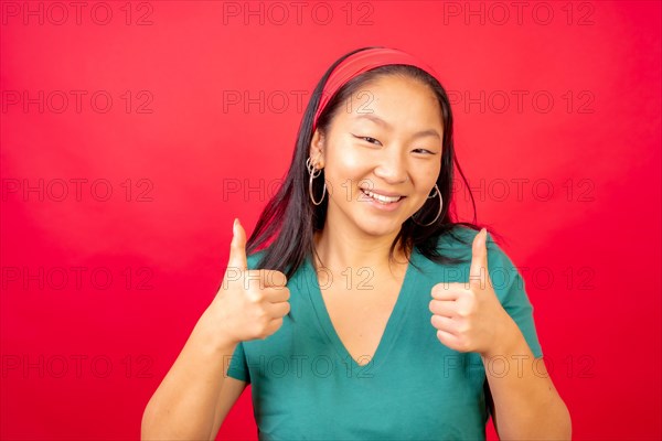 Studio photo with red background of a smiling chinese woman gesturing agreement with thumbs up