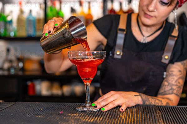 Professional bartender pouring a cocktail from shaker to glass in the counter of a bar