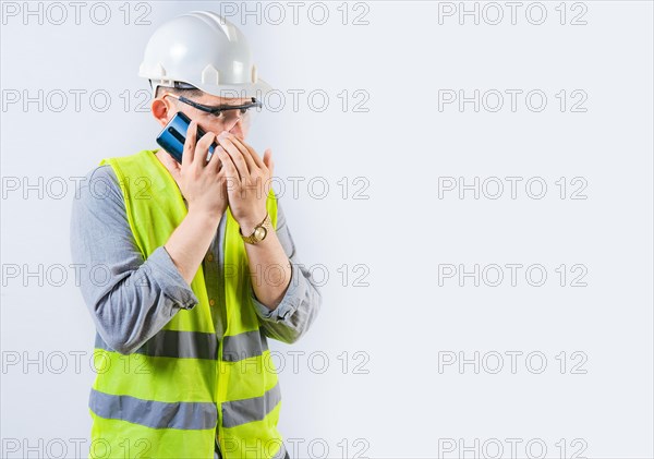 Male engineer talking on the phone secretly isolated. Young engineer in helmet talking on cell phone in silence