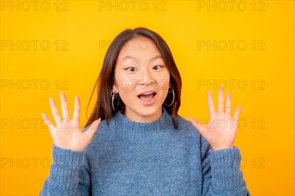 Studio photo with yellow background of a surprised chinese young woman looking at camera