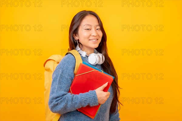 Studio photo with yellow background of a chinese student with headphones