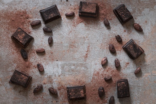 Overhead view broken chocolate bas with cocoa powder raw beans