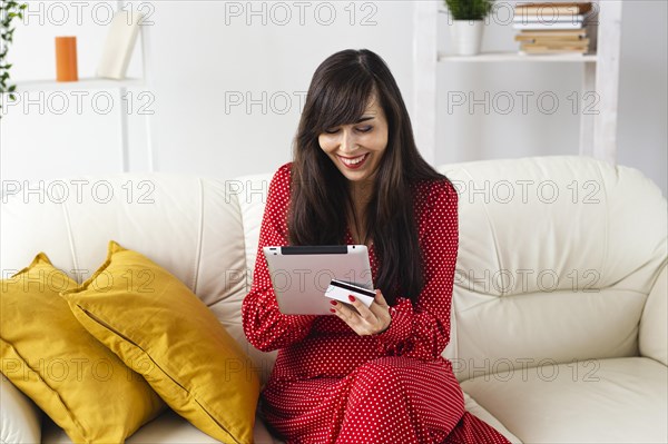 Front view smiley woman home ordering items sale using tablet credit card