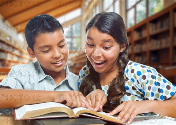 Two hispanic school kids having fun studying in a school library