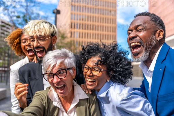 Happy and excited mature businesswoman taking a selfie and laughing with colleagues outdoors