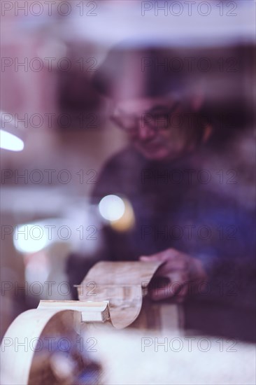 Senior expert luthier artisan violin maker carve sculpt chisel ribs of a new classical model cello in workshop Cremona Italy