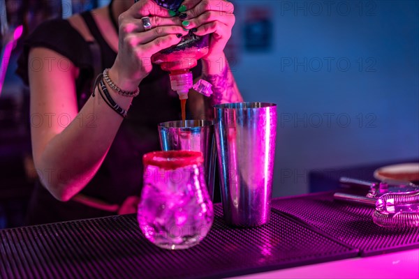 Bartender mixing ingredients in a cocktail mixer in the counter of a bar with neon lights