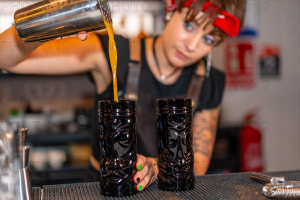 Concentrated young female bartender preparing creative cocktails in the bar counter