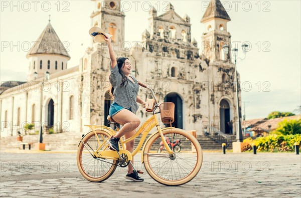 Lifestyle of a happy girl riding a bicycle holding her hat on the street. Happy young woman in hat riding a bicycle on the street. Granada