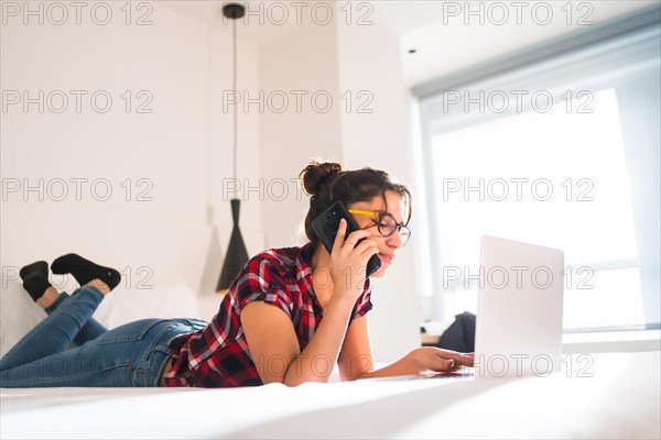 Smart young woman working using phone and laptop from an hotel room