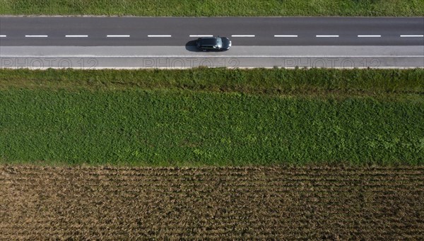 Drone view of a country road with a car between harvested fields