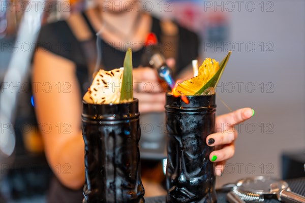 Bartender using an electric torch to flaming the garnish of a cocktail in the counter of a bar