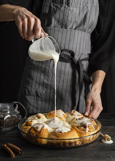 Close up hand pouring cream cinnamon rolls