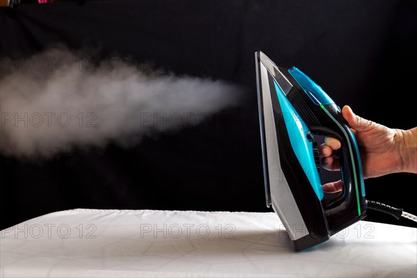 Woman ironing a white cloth by pouring steam from the iron on a black background