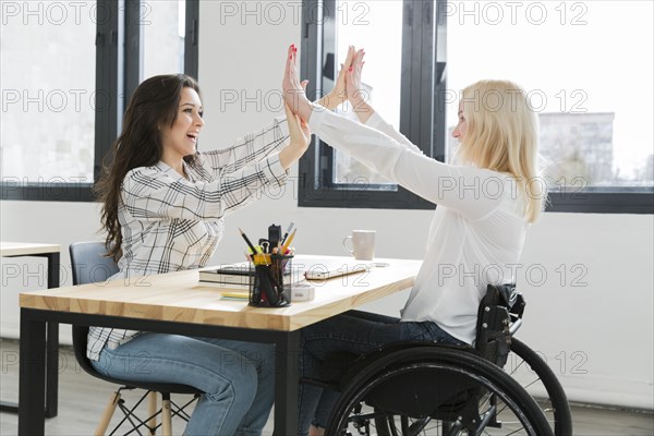 Woman wheelchair high fiving with her colleague