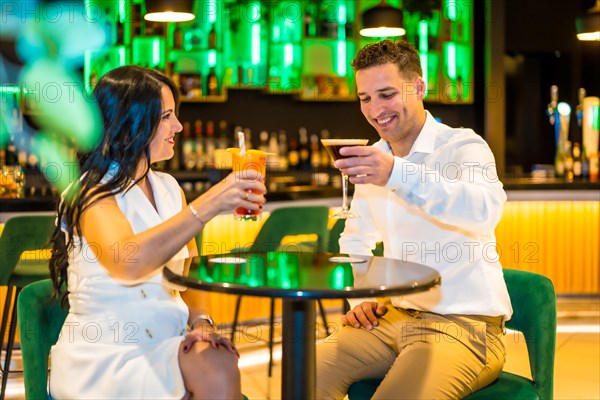 Happy couple toasting with cocktails sitting on a luxury bar