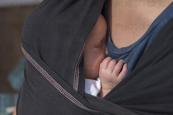 Baby sleeping in a sling with his mother