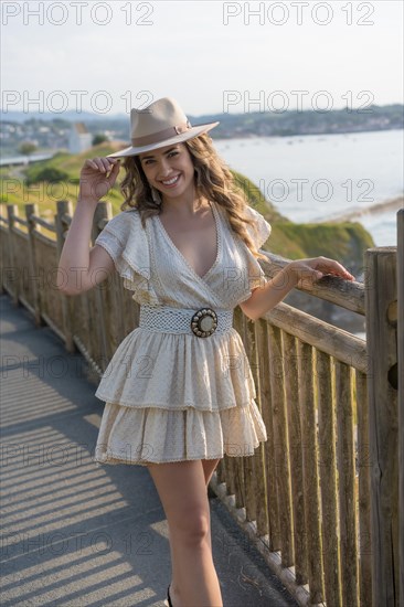 Vertical portrait of a woman wearing summer dress and hat posing next to the sea