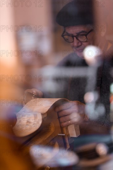 Senior expert luthier artisan violin maker carve sculpt chisel ribs of a new classical model cello in workshop Cremona Italy