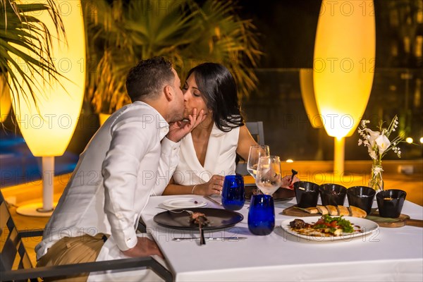 Romantic scene of a couple kissing during dinner in a luxury terrace of a restaurant