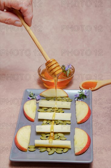 Woman sprinkles a wooden spoon with honey on a tray with cheese