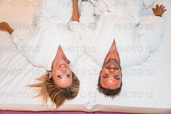 From above two people lying on a luxury bed wearing white bathrobe
