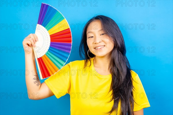 Studio photo with blue background of a chinese woman using a rainbow colored folding fan
