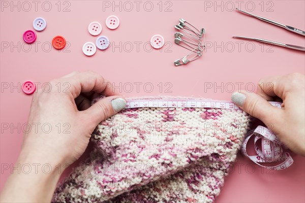 Close up woman s hand measuring knitted fabric with buttons safety pins crochet needle