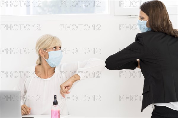 Coworkers wearing masks elbow bump each other