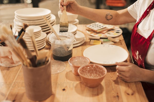 Female taking ceramic color paint plate with brush