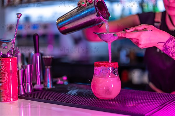 Cropped close-up photo of a woman mixing ingredients of a cocktail in the counter of a nightclub