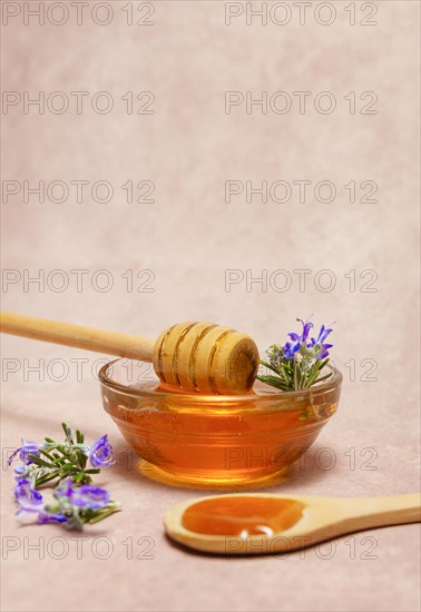 Honey in a glass bowl with a wooden spoon and fresh rosemary sprigs in bloom