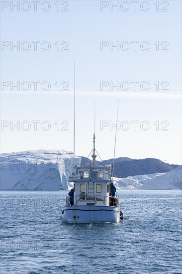 An excursion boat in the UNESCO World Heritage Ilulissat Icefjord sails towards a huge iceberg. Ilulissat