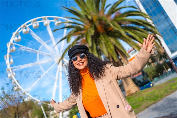 Happy fashionable latin woman next to a Ferris wheel in a sunny day of winter in the city