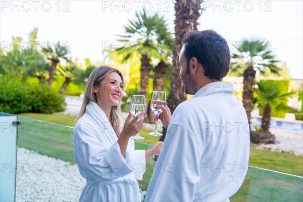 Happy caucasian couple wearing bathrobe toasting standing on a luxury room terrace hotel