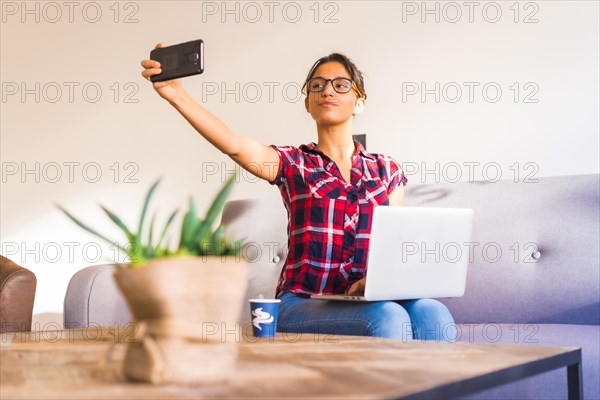 Freelancer taking a selfie while working at home using laptop sitting on a sofa