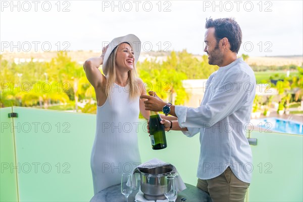 Newlywed couple celebrating honeymoon with champagne standing on the terrace of a hotel