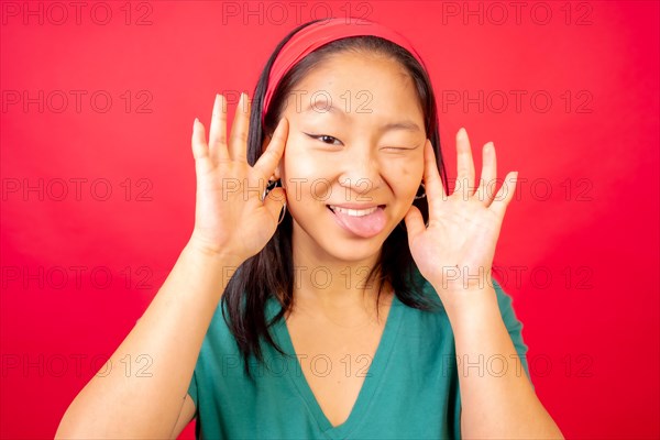 Studio photo with red background of a funny chinese young woman pulling faces and gesturing