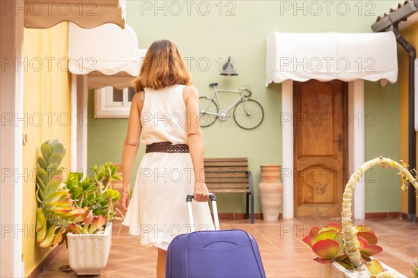 Rear view of a woman carrying suitcase arriving home from holidays