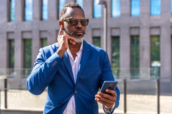Cool african businessman using earphones to talking to the mobile standing outdoors in the financial district