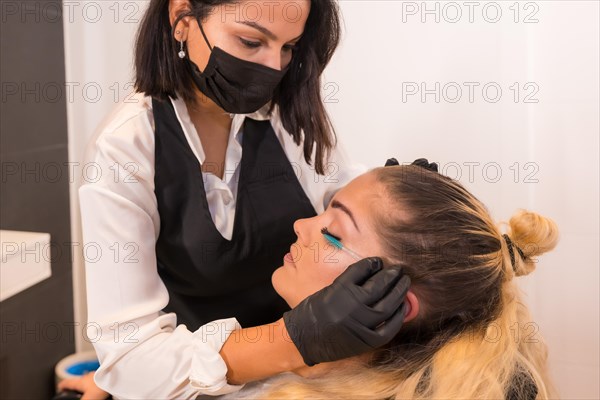 Profile close-up photo of a professional aesthetician brushing the eyelashes to a client