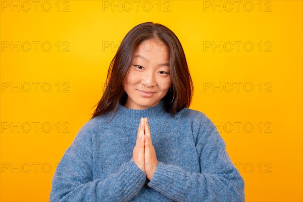 Asian woman making the please gesture looking at camera on a yellow background