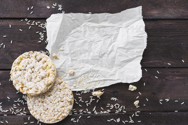 Crumpled paper with two round puffed rice cake with grains wooden desk