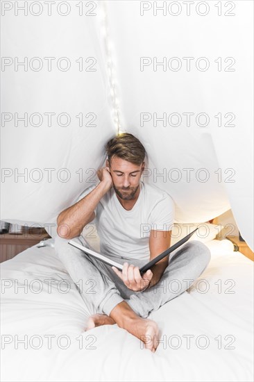 Man sitting inside curtain looking album bed
