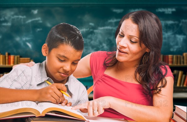 Female school teacher tutoring a young hispanic boy in the classroom