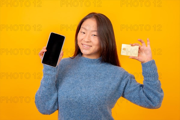 Studio photo with yellow background of a chinese woman using credit card to shop online