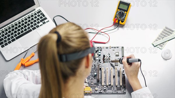 High angle female technician with soldering iron electronics motherboard