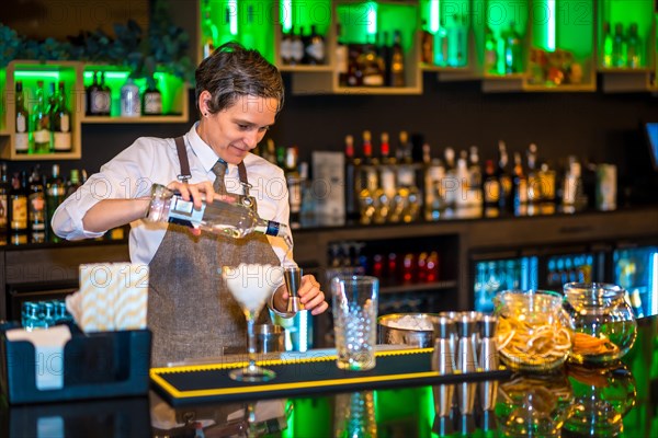 Bartender pouring alcohol in a measuring dispenser to prepare a luxury cocktail